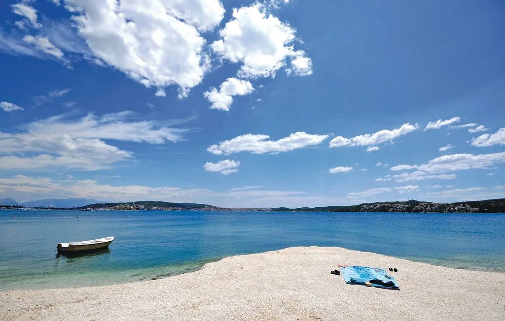 Una playa de arena junto a aguas azules tranquilas bajo un cielo nublado.