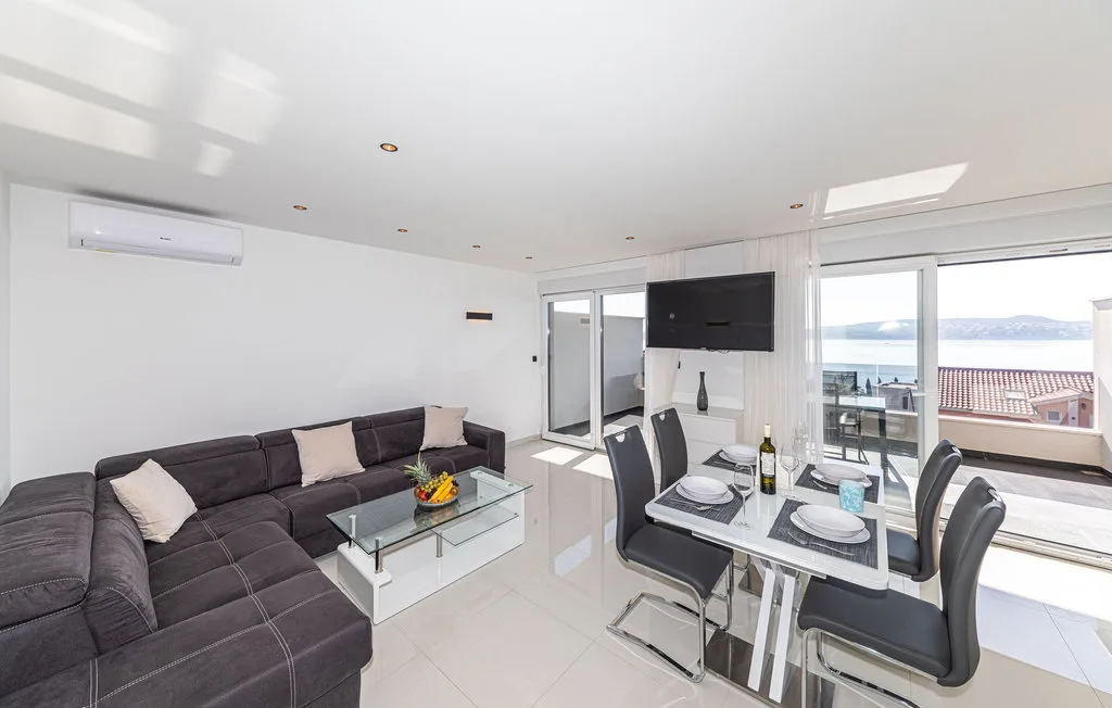 Una luminosa sala de estar y comedor tiene asientos oscuros y grandes ventanales con vistas al agua.