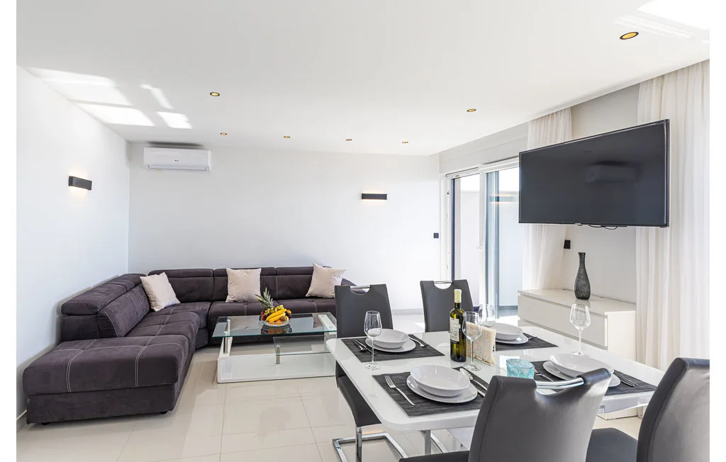 Sala de estar y comedor con asientos seccionales y un televisor montado en la pared.
