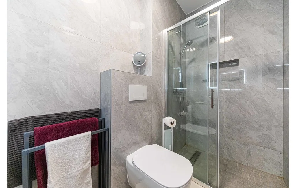 Un baño con azulejos, una ducha de vidrio y un inodoro suspendido.
