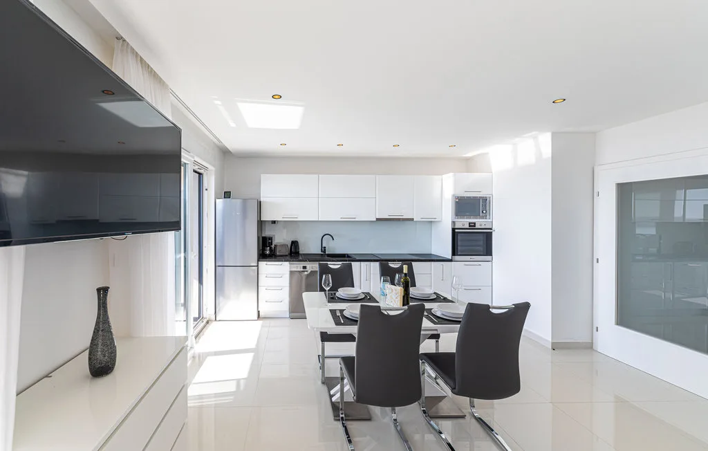 Una luminosa cocina-comedor de concepto abierto con una mesa y gabinetes blancos.