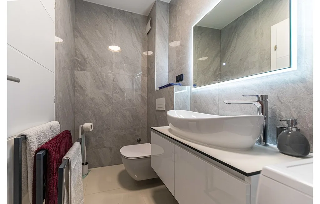 Un baño moderno con lavabo sobre encimera, inodoro y espejo iluminado.