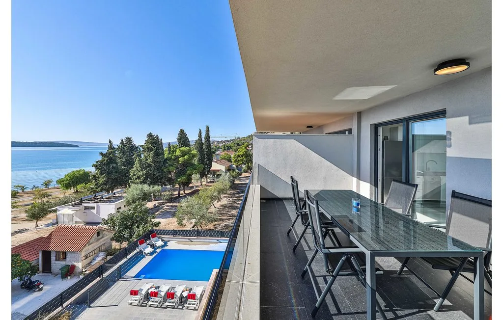 Una zona de comedor en un balcón da a una piscina, árboles y el agua.