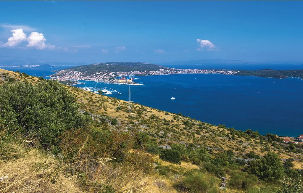Una ladera costera domina una bahía azul y una costa distante.