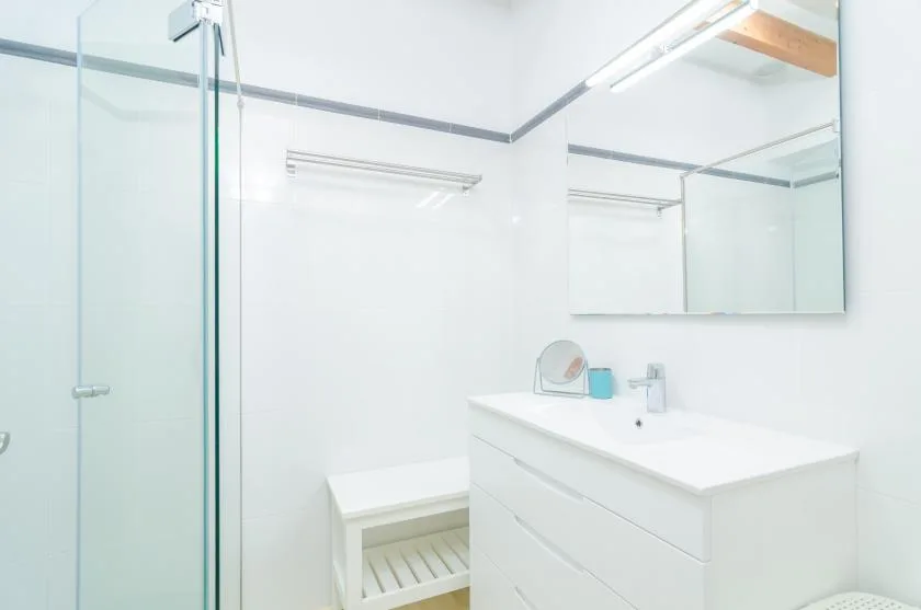 A bright bathroom with a glass shower, sink, and wall mirror.