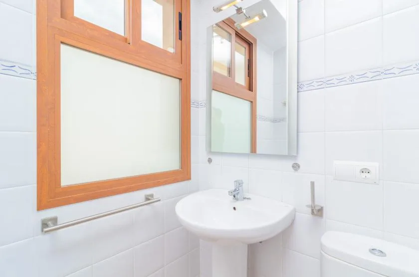 A tiled bathroom with a pedestal sink, mirror, and wooden-framed window.