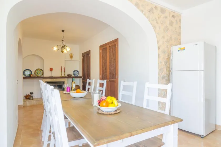 A dining area with a long table, white chairs, and a refrigerator.