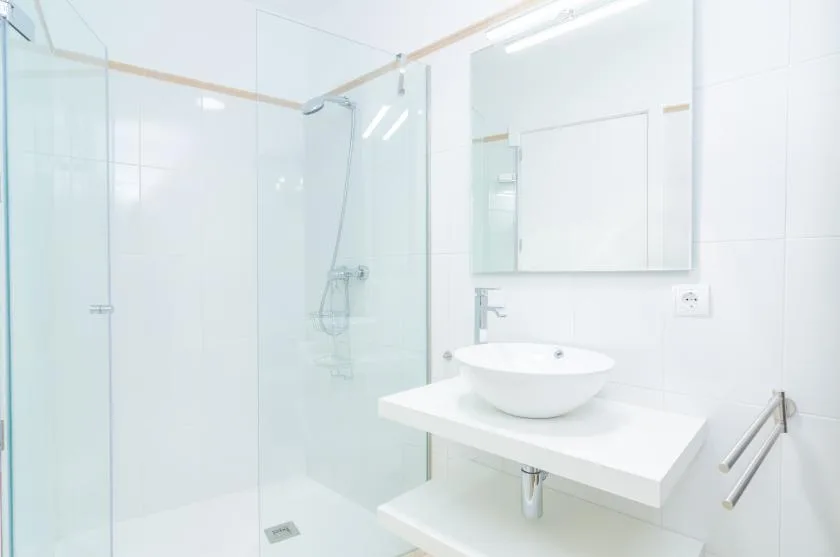 A bright white bathroom with a glass shower and a sink on a wall-mounted counter.
