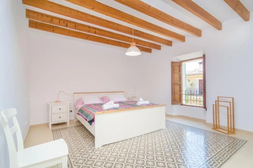 A bright bedroom with a bed beneath exposed wooden ceiling beams.
