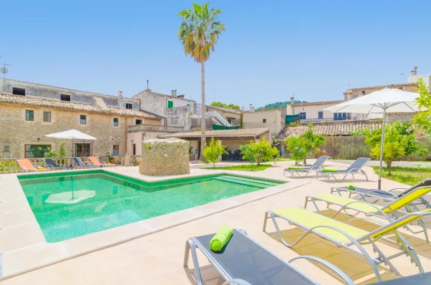 Una piscina al aire libre está rodeada de tumbonas y edificios bajos de piedra.