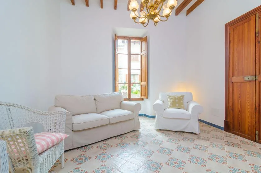 A bright sitting room with a sofa, an armchair, and a tall window.