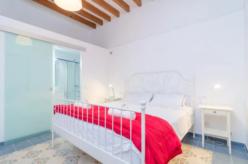 A bedroom with a white bed, bright red blanket, and bedside tables.