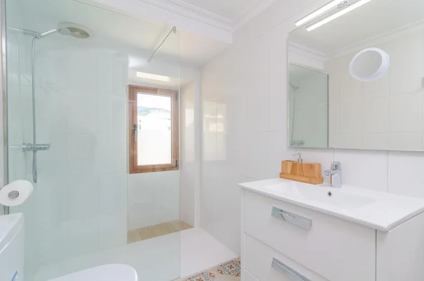A bright bathroom with a glass shower, a window, and a white vanity.