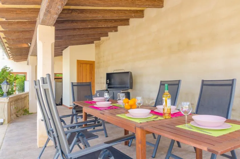 Un comedor exterior cubierto con una mesa larga preparada con platos y fruta.
