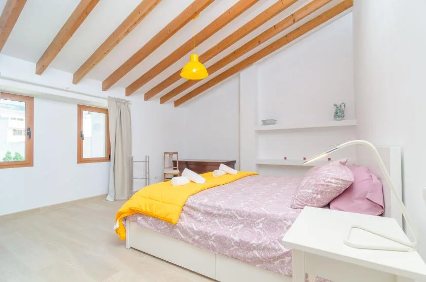 A bright bedroom with a bed dressed in pink bedding and a yellow throw.