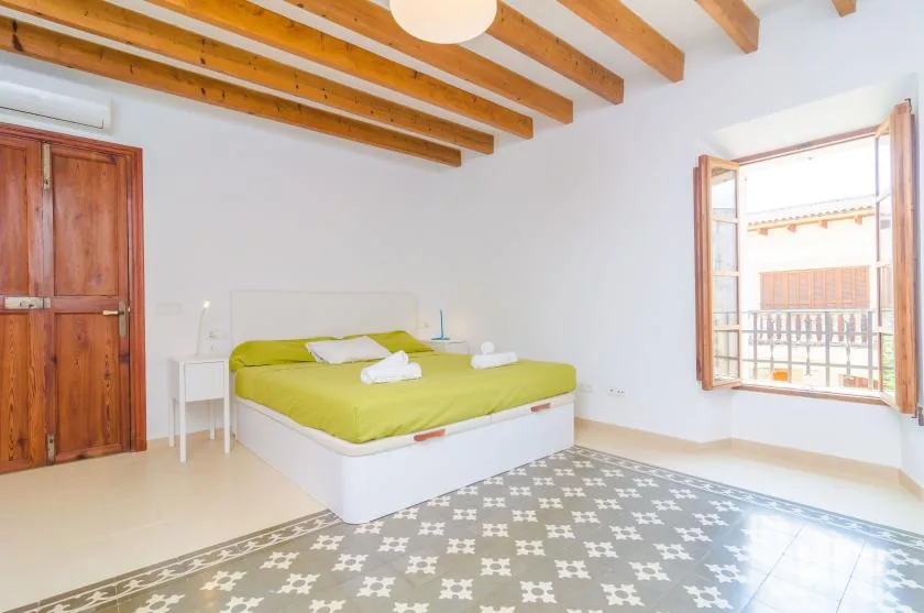 A bright bedroom with a bed beneath exposed wooden ceiling beams.