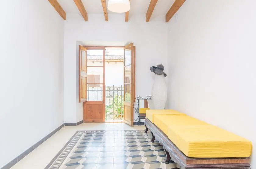 A bright bedroom with yellow bedding and open wooden doors leading to a balcony.