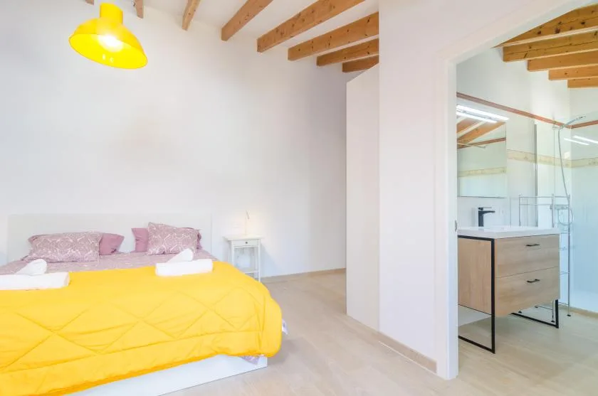 A bedroom with a bed covered by a bright yellow bedspread and an adjoining bathroom.