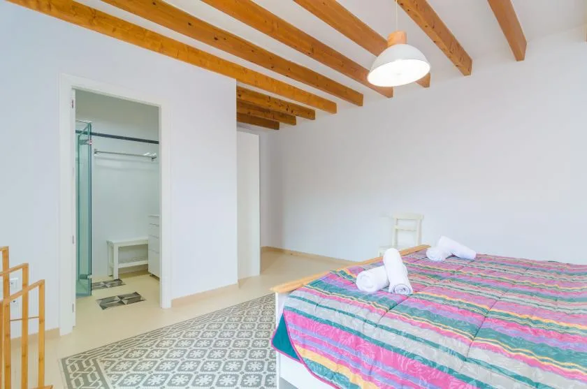 A bedroom with a colorful striped bedspread beneath exposed wooden ceiling beams.