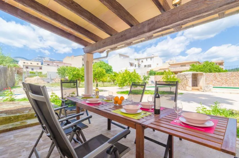 Un patio exterior cubierto tiene una mesa puesta junto a asientos de jardín.