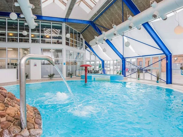 An indoor swimming pool with a water spout and large windows.