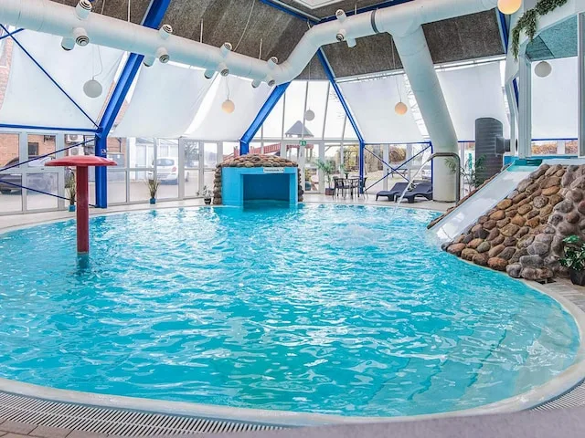An indoor swimming pool with a rocky feature and large windows.