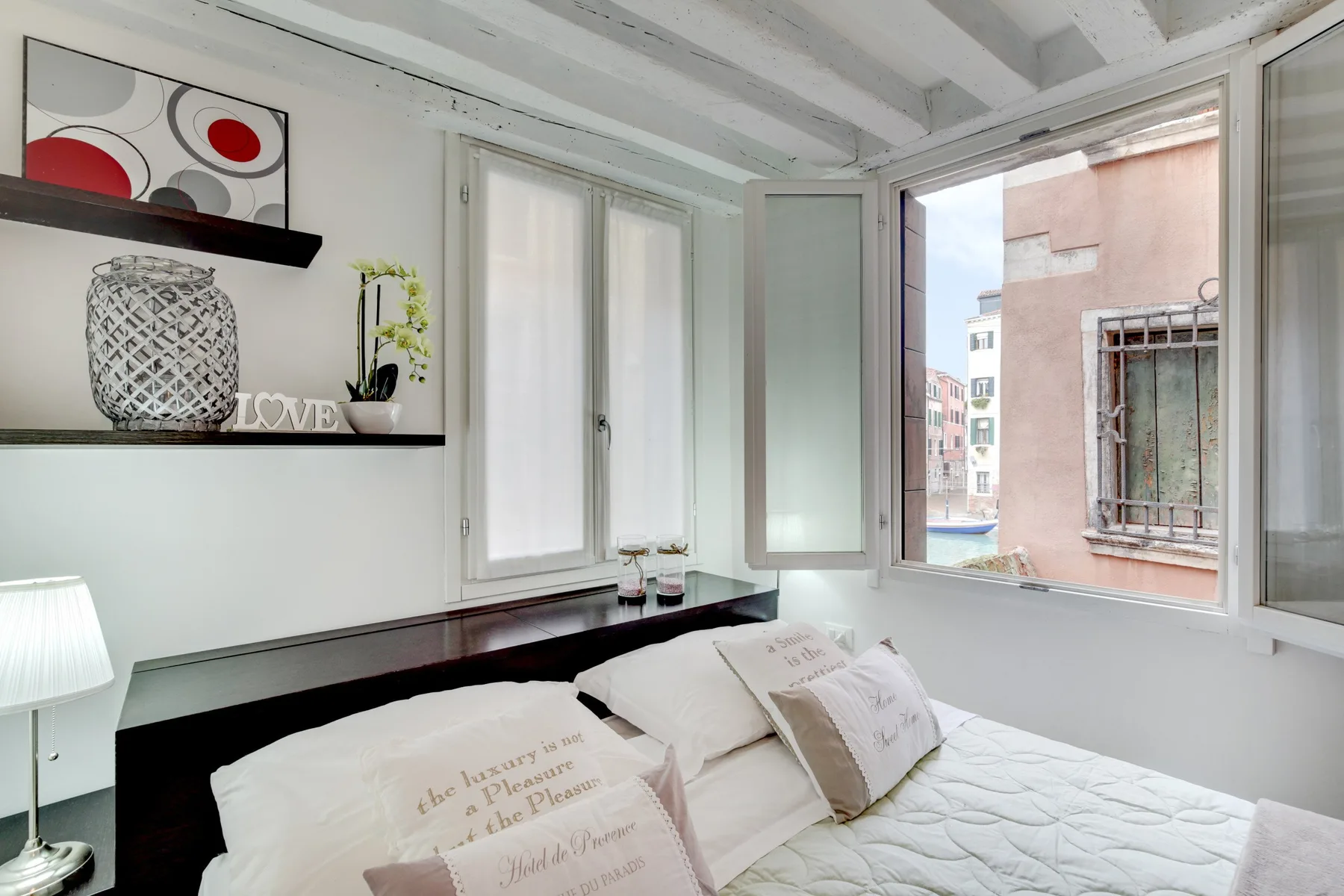 Un dormitorio luminoso con una cama, estantes en la pared y una ventana abierta.