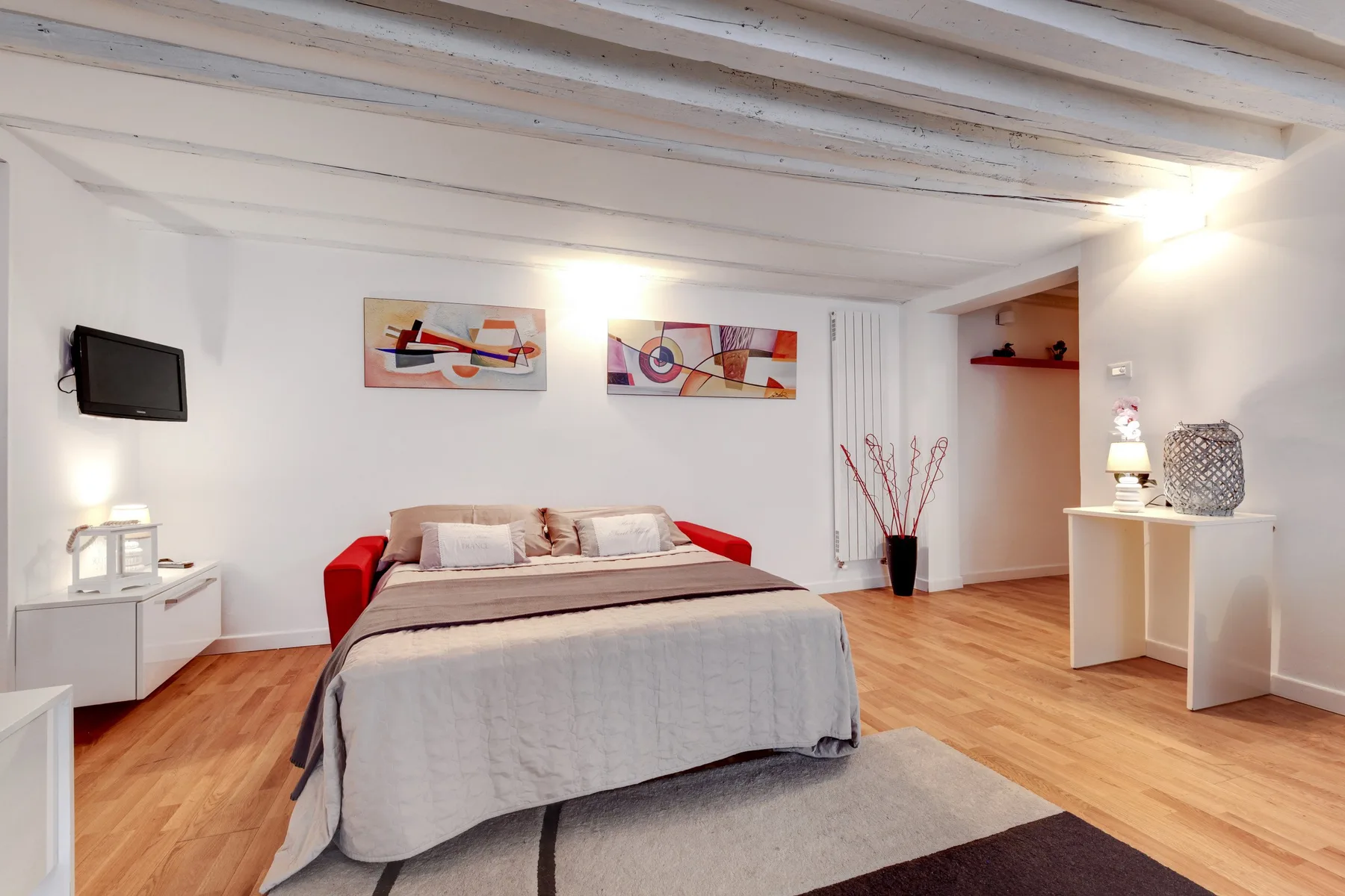 Un dormitorio con una cama, un televisor en la pared y obras de arte coloridas.