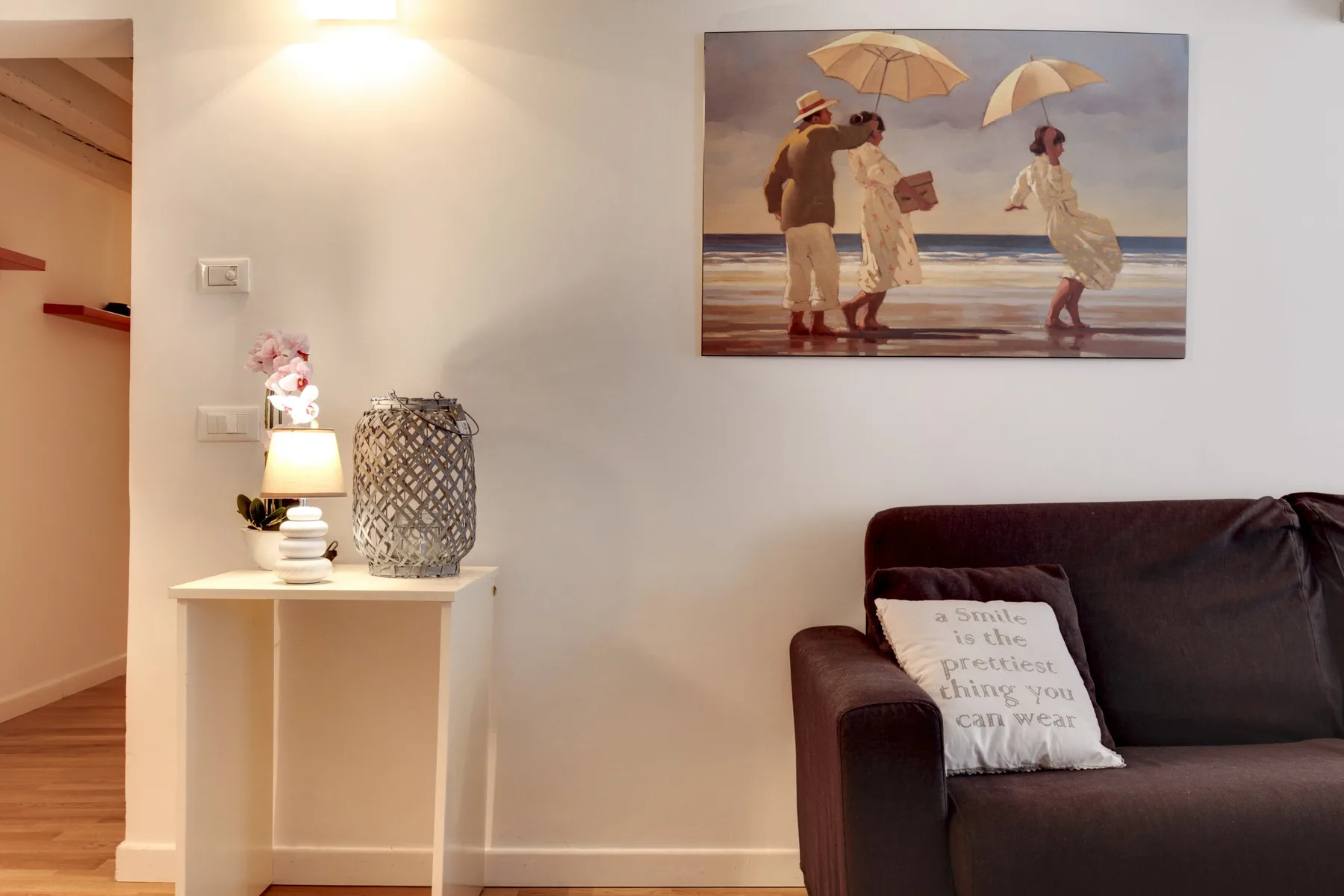 Una sala de estar con un sofá oscuro y una obra enmarcada de playa en la pared.