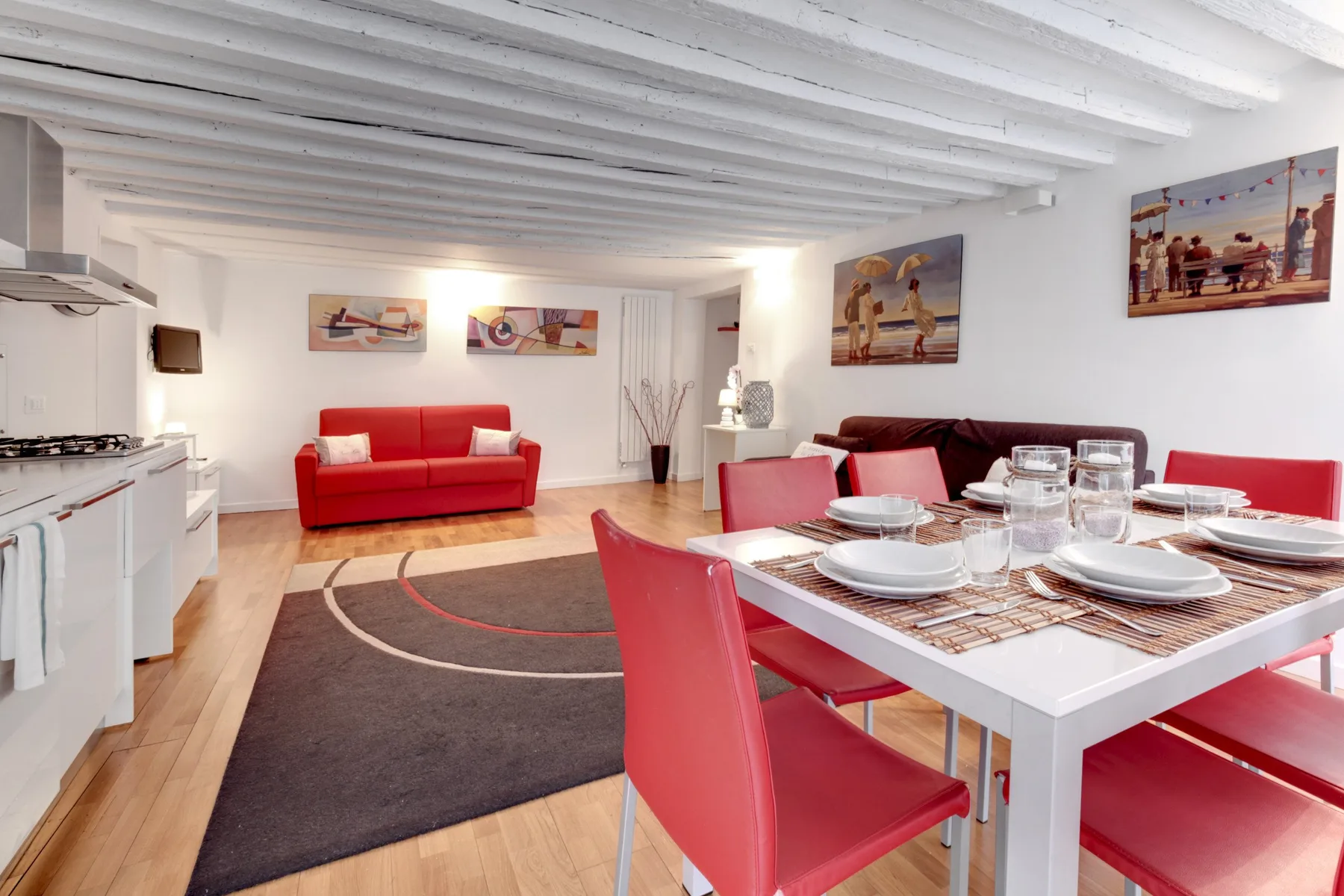 Una luminosa sala-comedor tiene la mesa puesta junto a un sofá rojo.