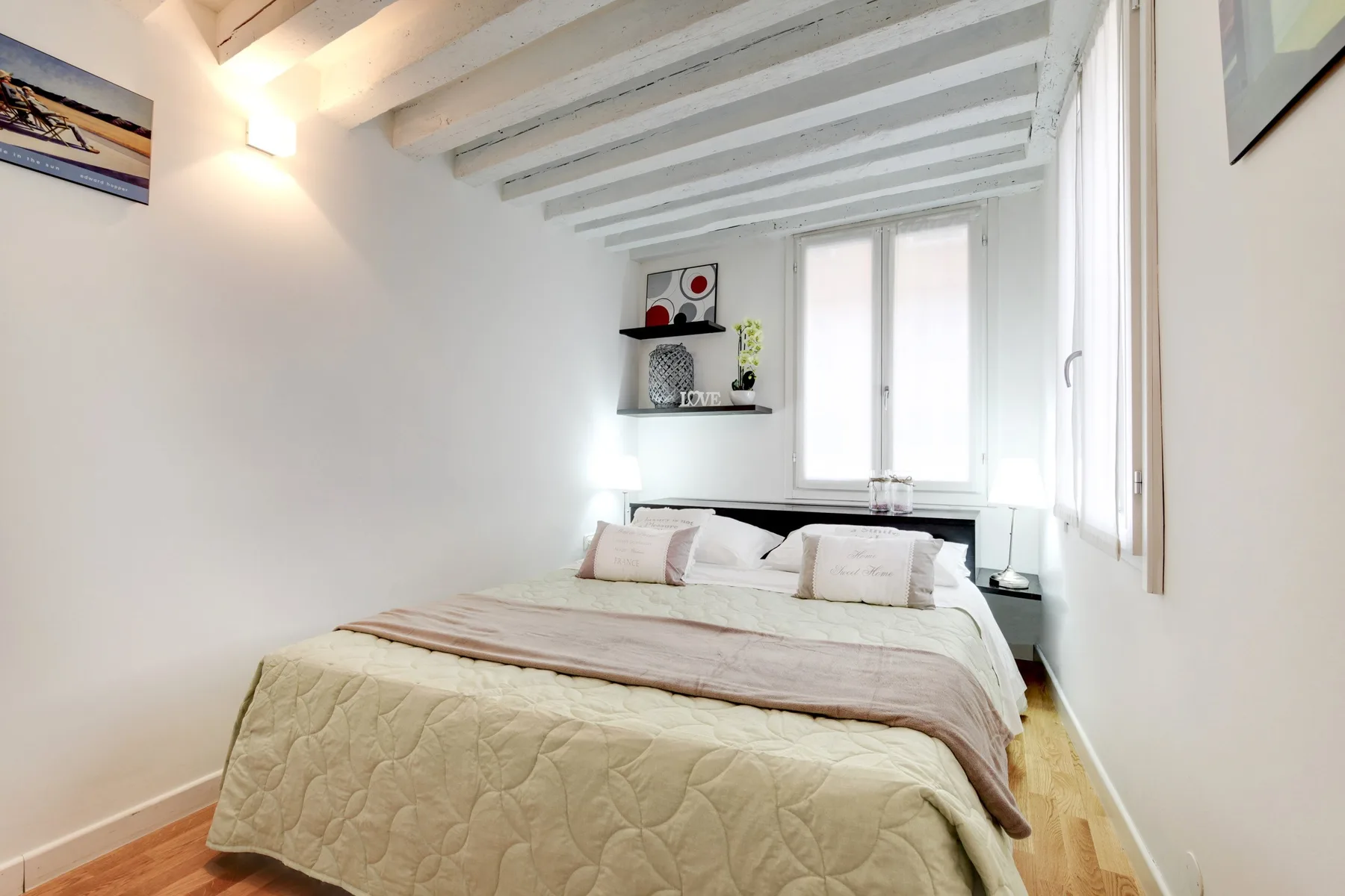 Un dormitorio luminoso con una cama bajo vigas blancas y una ventana.