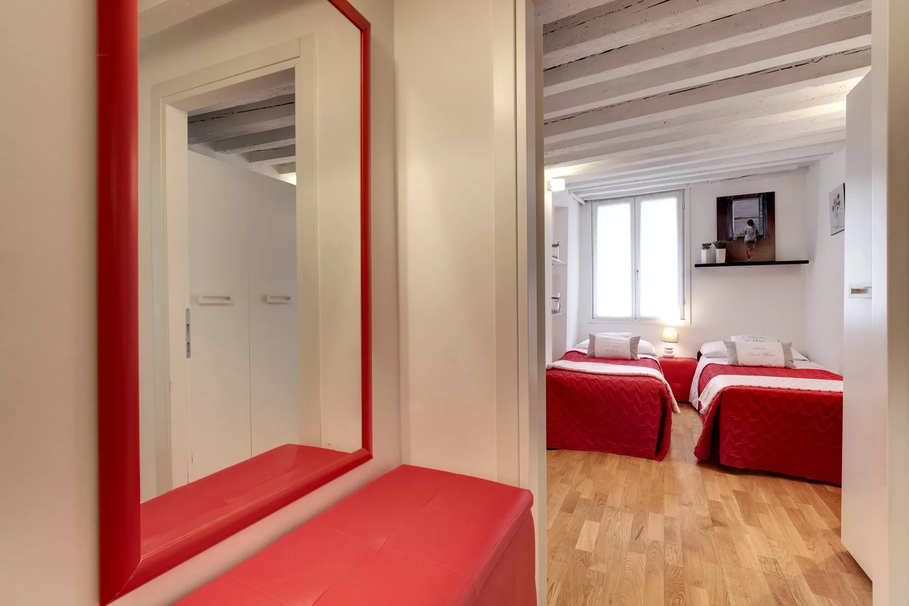 Un dormitorio luminoso con ropa de cama roja y suelo de madera.