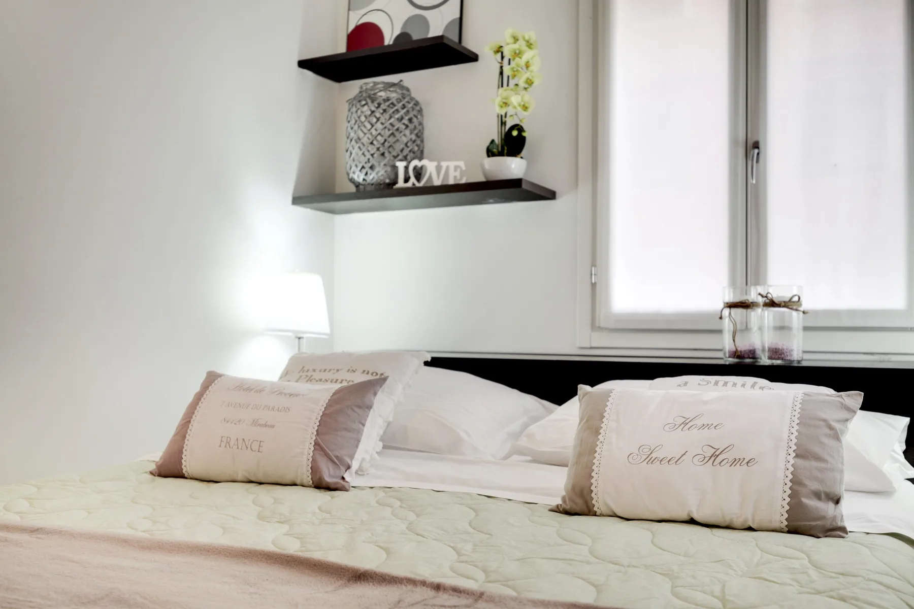 Un dormitorio con una cama bien tendida y cojines decorativos bajo una ventana.