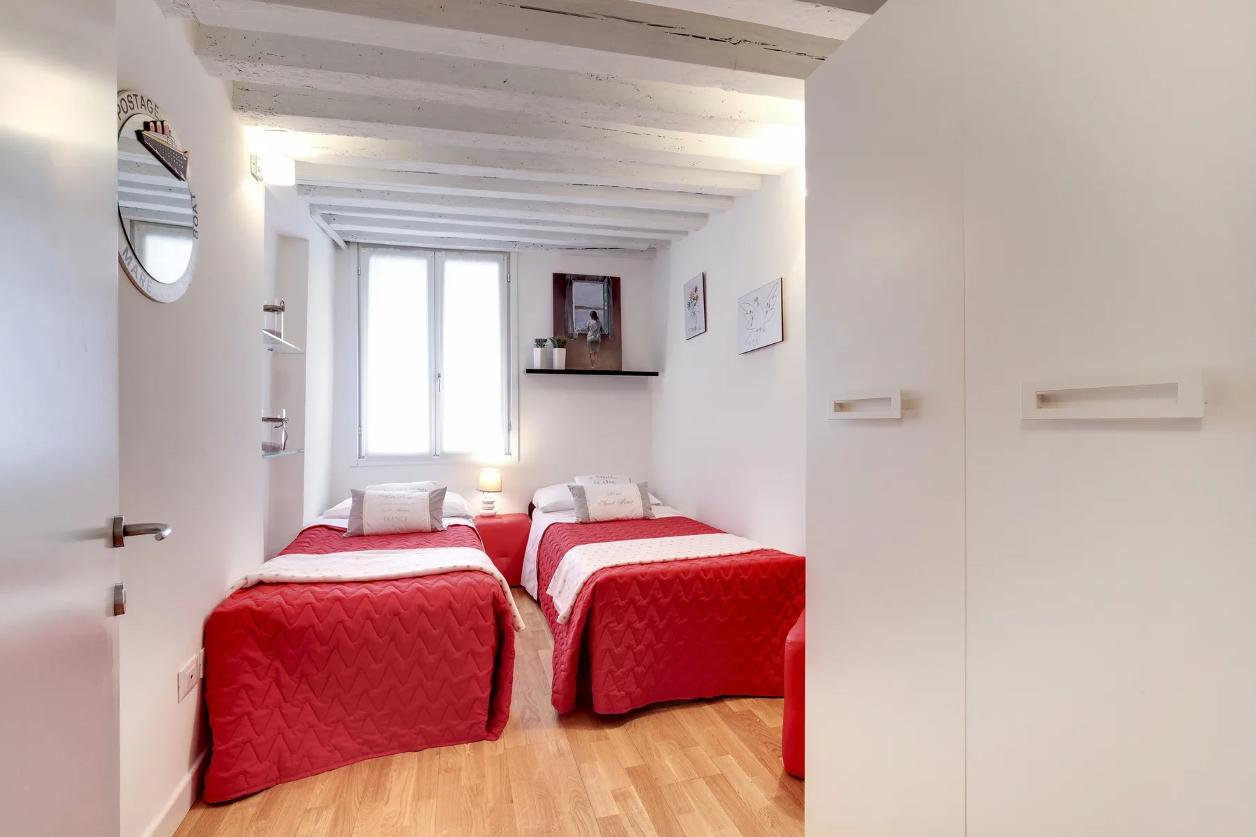Un dormitorio luminoso con dos camas vestidas con colchas rojas.
