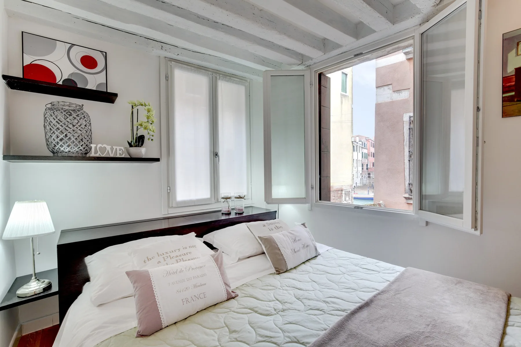 Un dormitorio con una cama, almohadas y una ventana abierta.