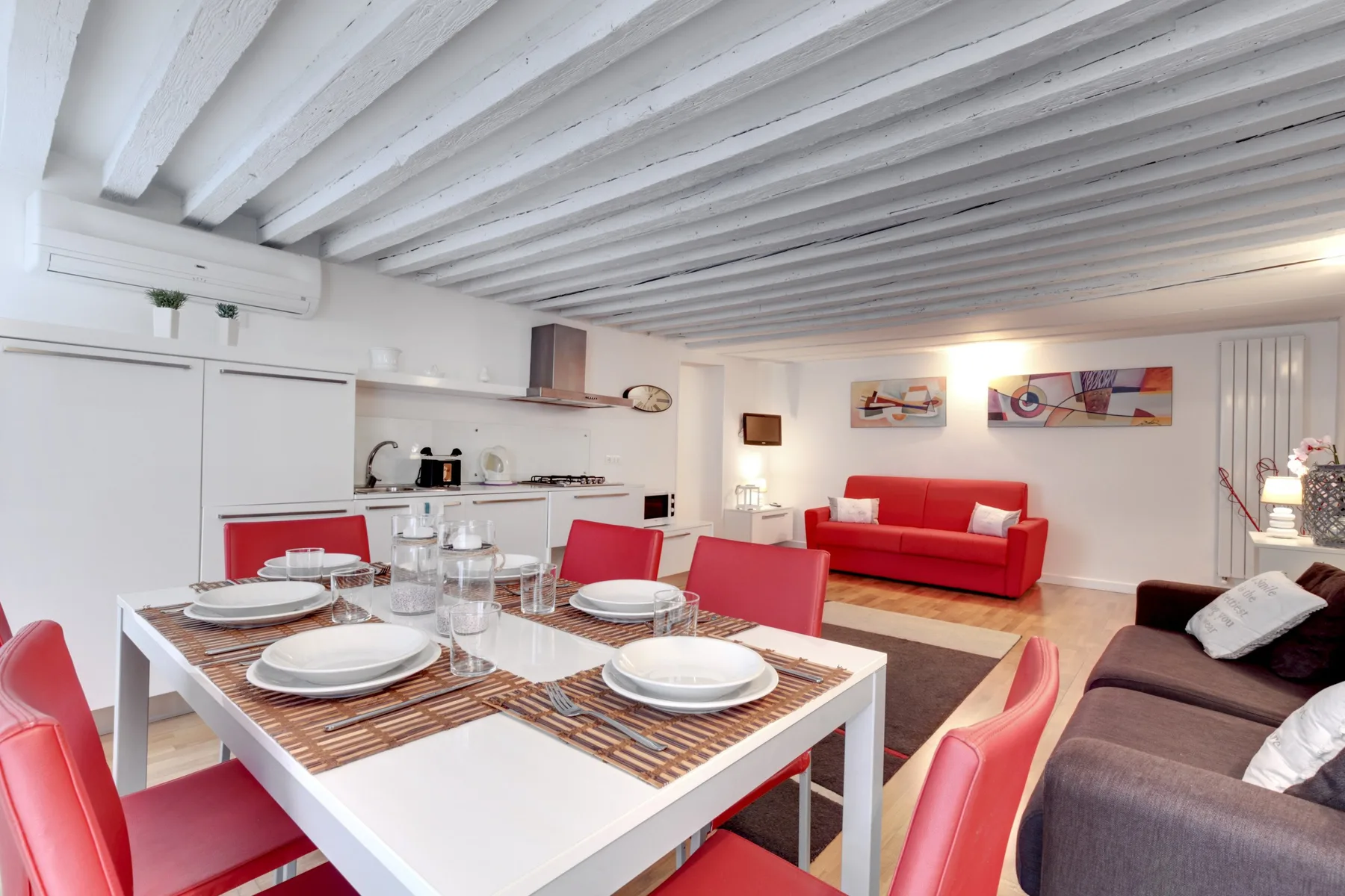Comedor con la mesa puesta, junto a una sala de estar con asientos rojos.