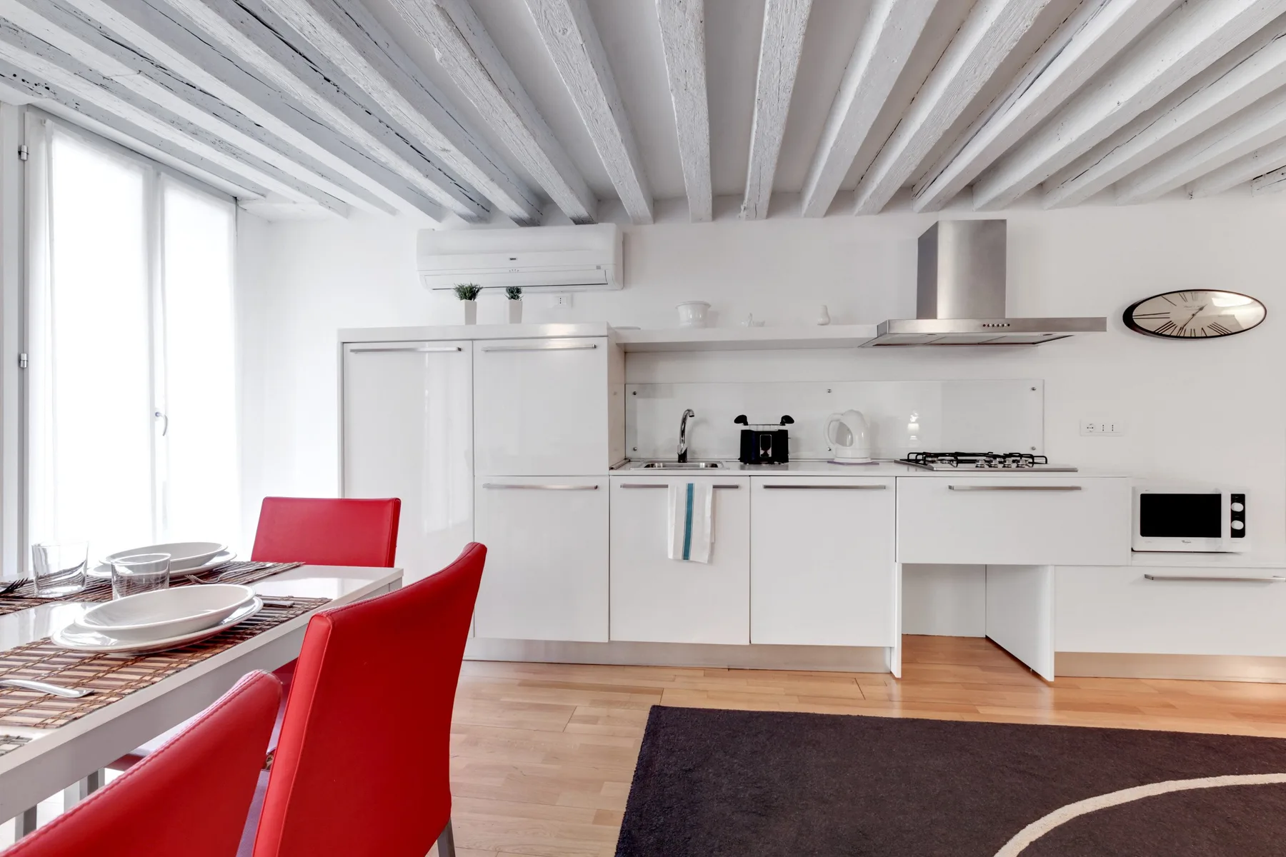 Una cocina y comedor luminosos con gabinetes blancos y asientos rojos.