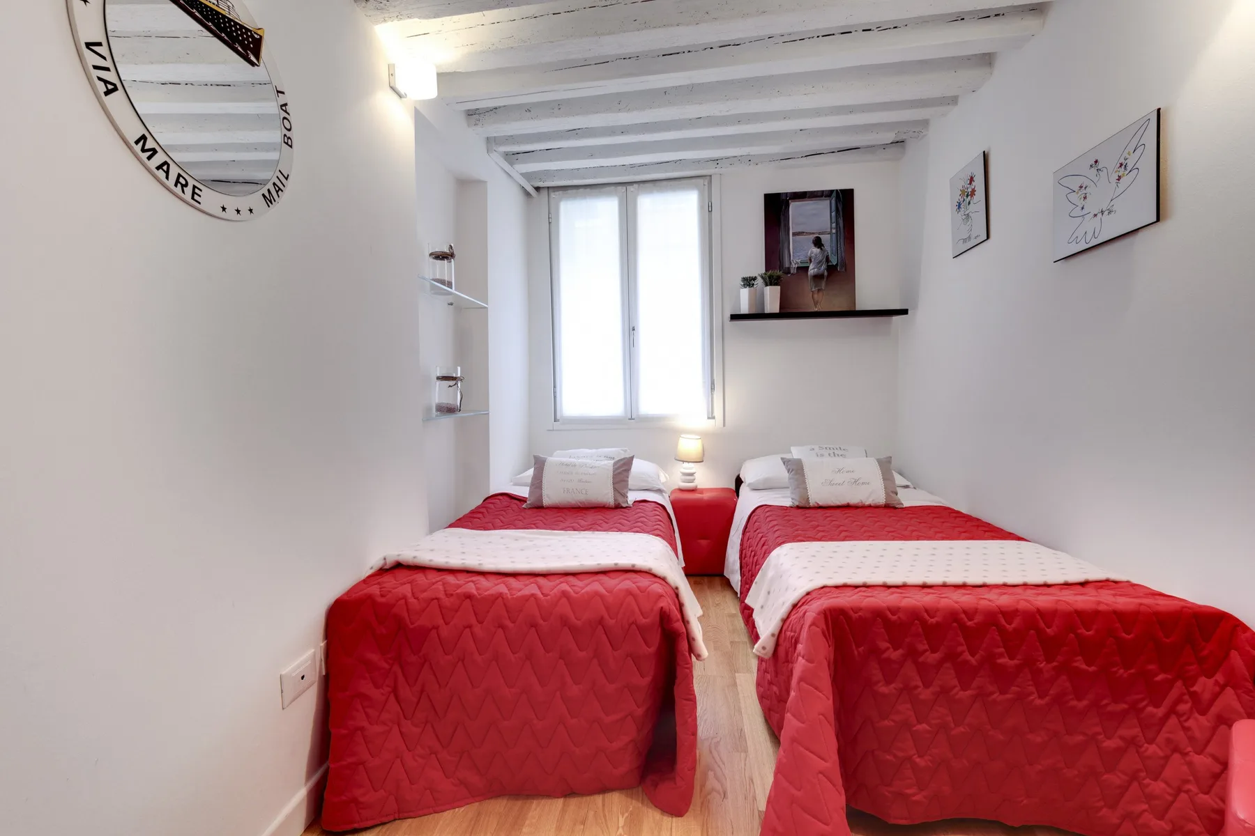 Un dormitorio con dos camas cubiertas con ropa de cama roja bajo una ventana luminosa.