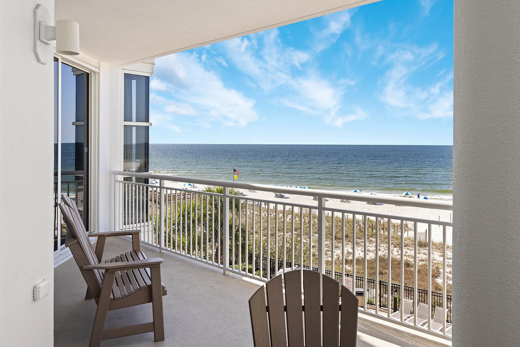 A balcony overlooks the beach and ocean, with seating beside the railing.
