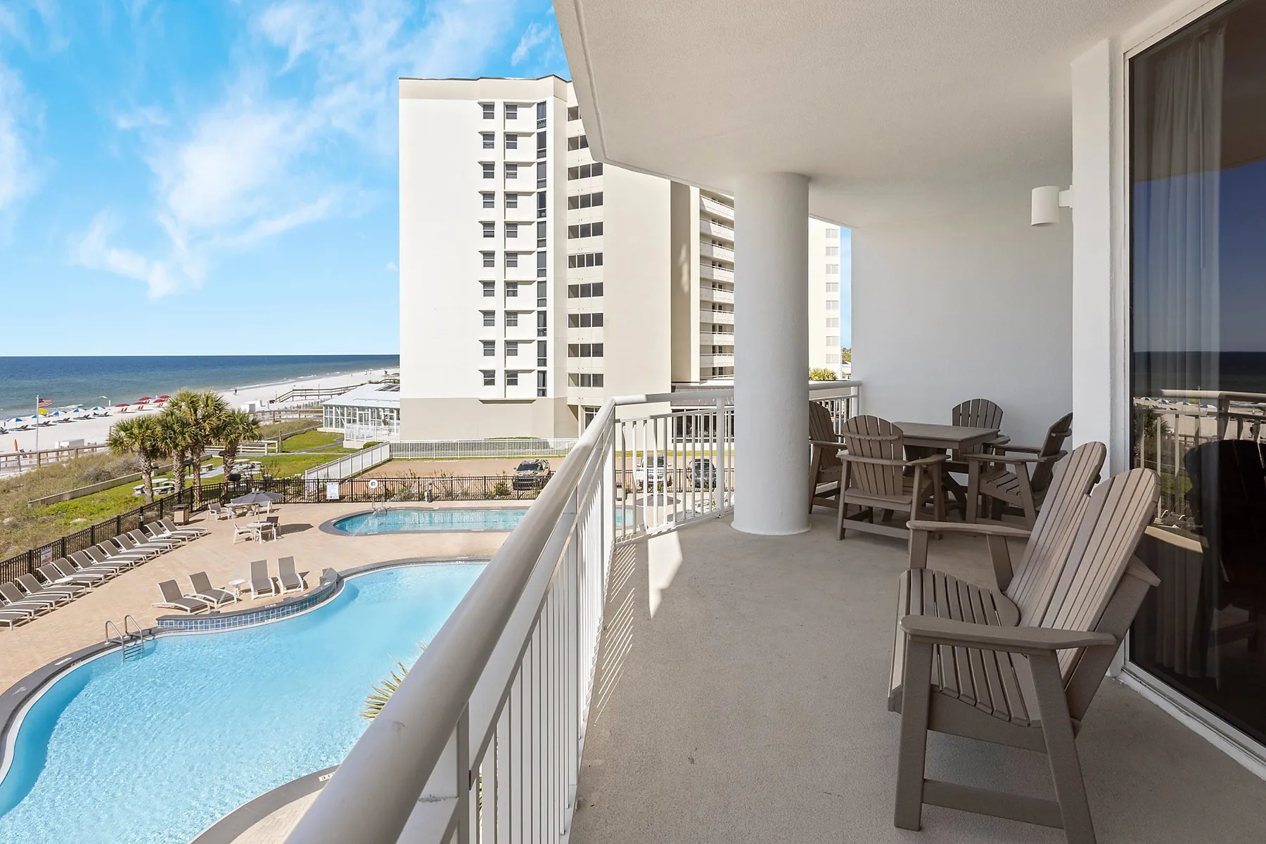 A balcony with seating overlooks a swimming pool and the ocean.