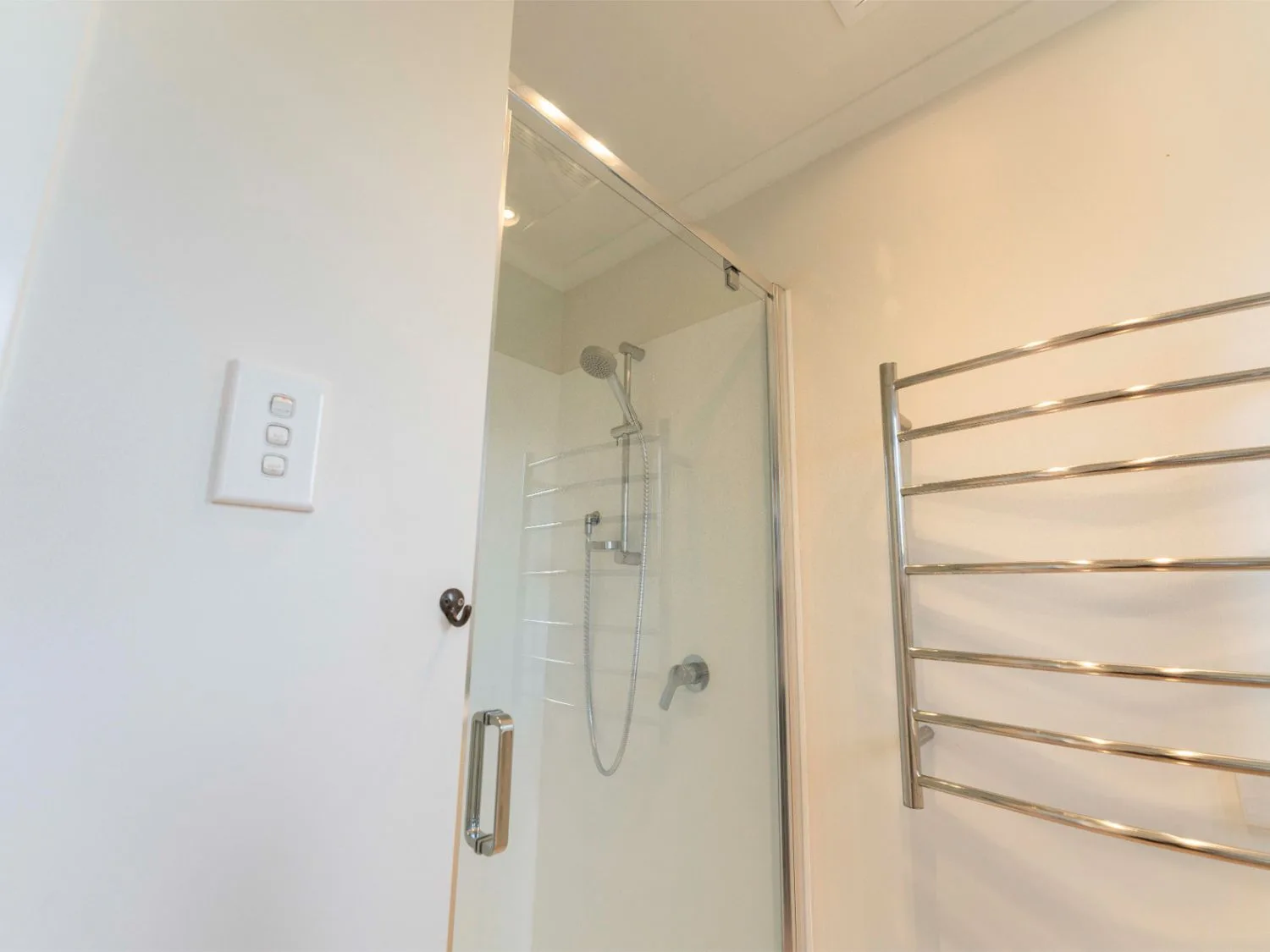 Una ducha de baño con panel de vidrio y un toallero calefactado.