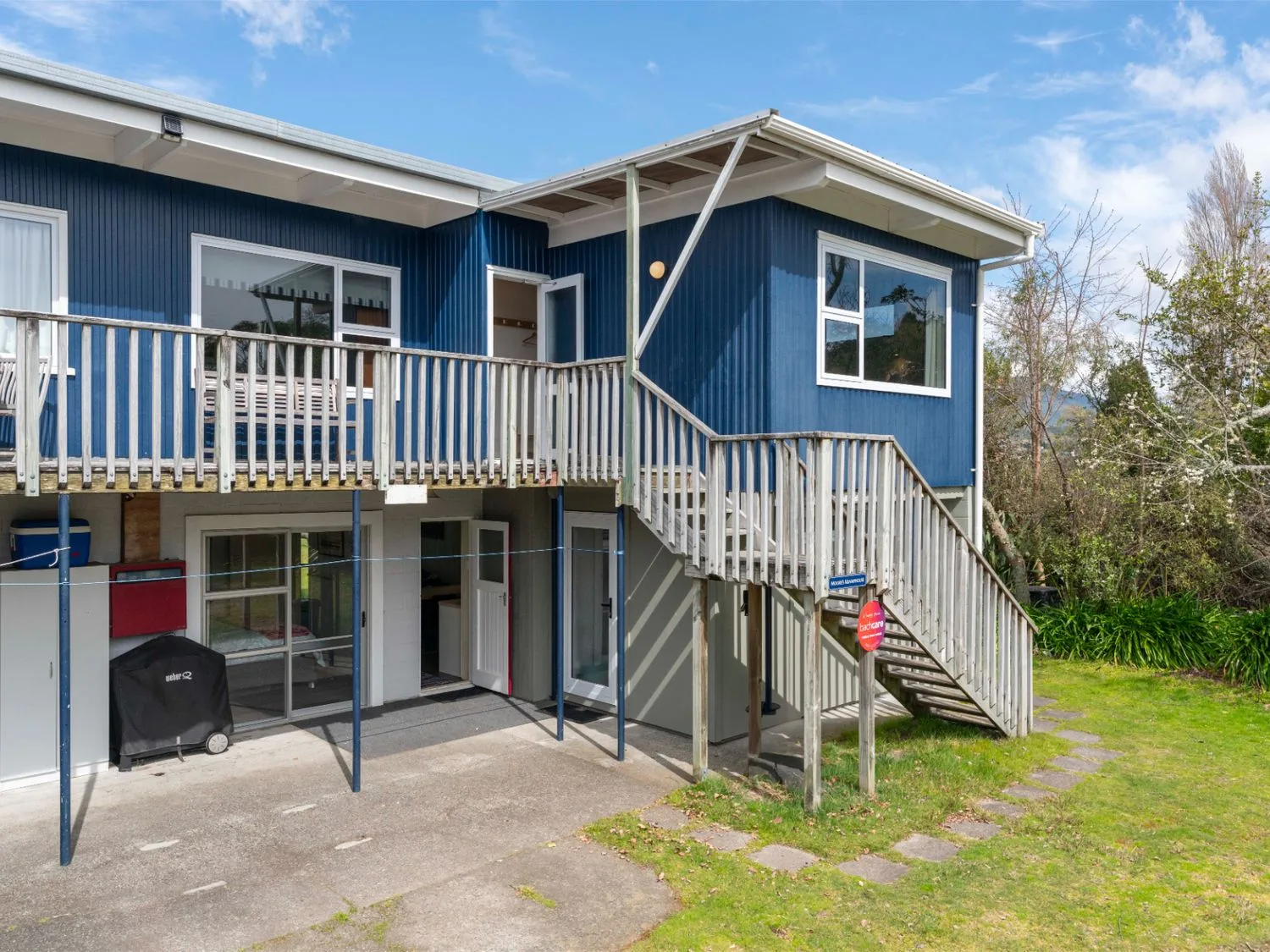 Casa azul de dos pisos con una terraza elevada de madera y escaleras exteriores.