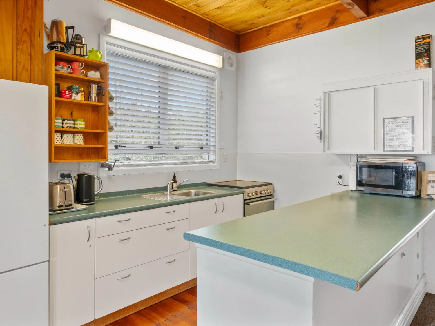 A kitchen with green countertops, white cabinets, and a window with blinds.