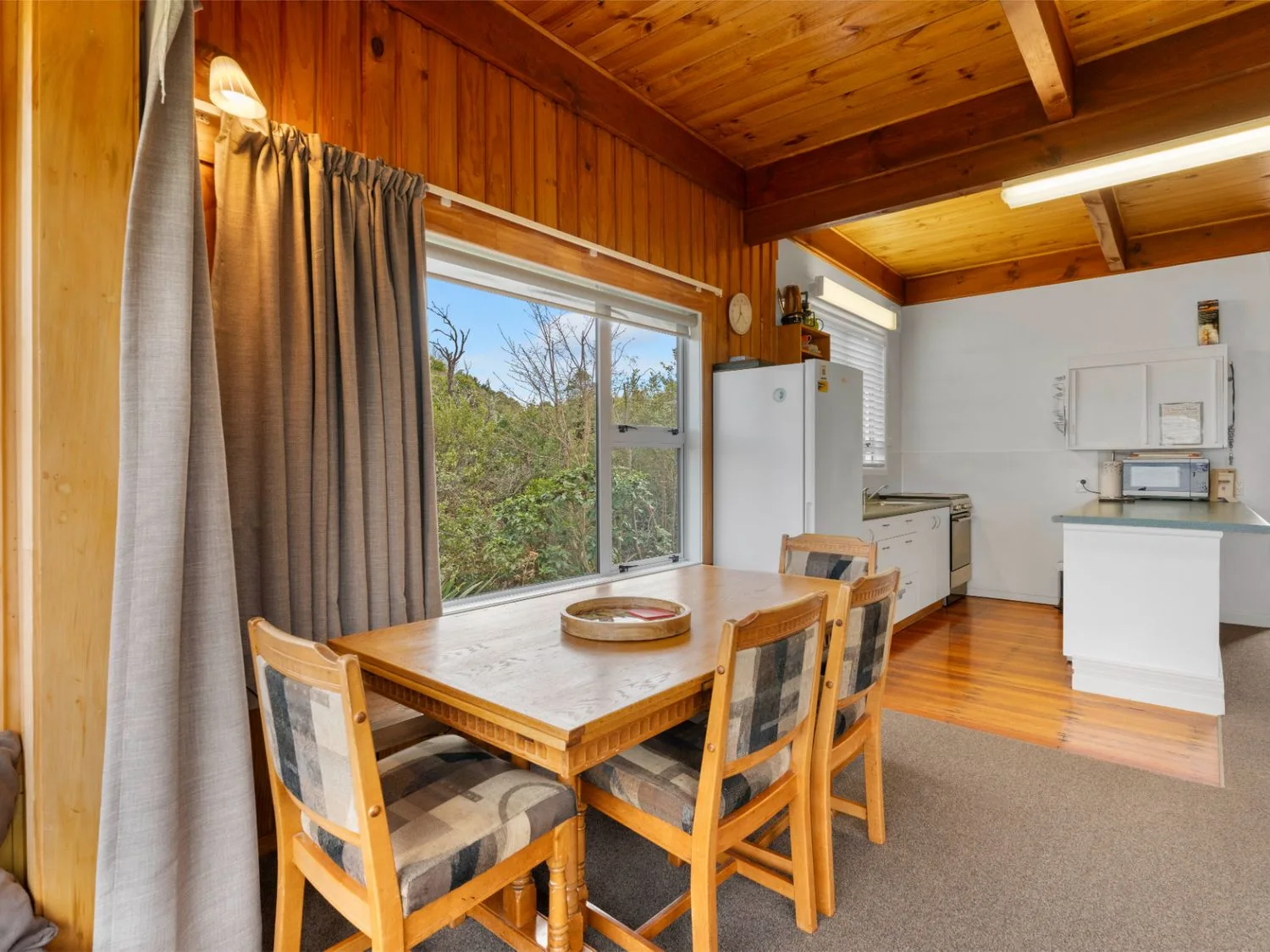 Un comedor con una mesa de madera junto a una ventana grande, conectado con una cocina.