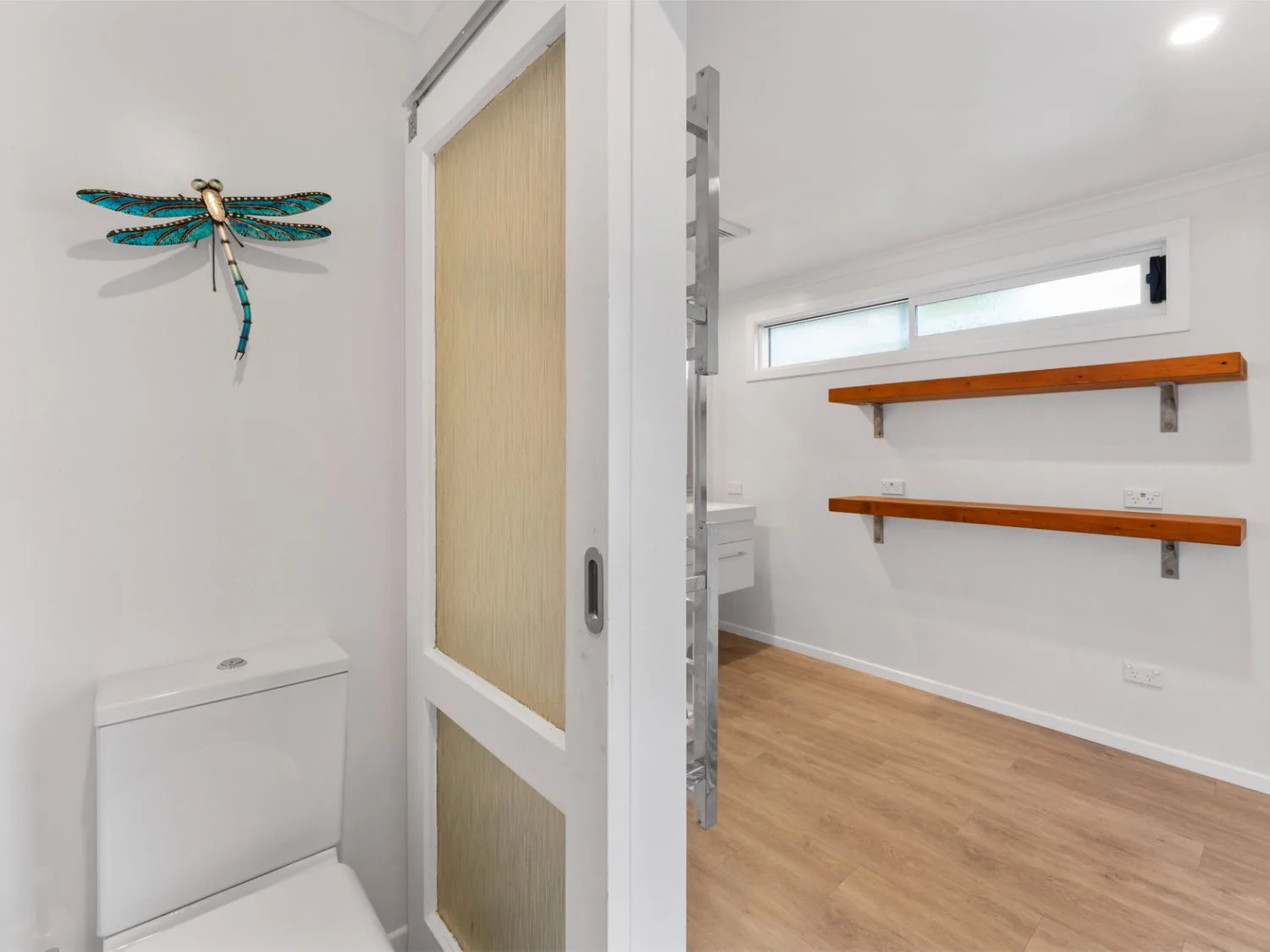 Un baño con un inodoro y una libélula decorativa en la pared.