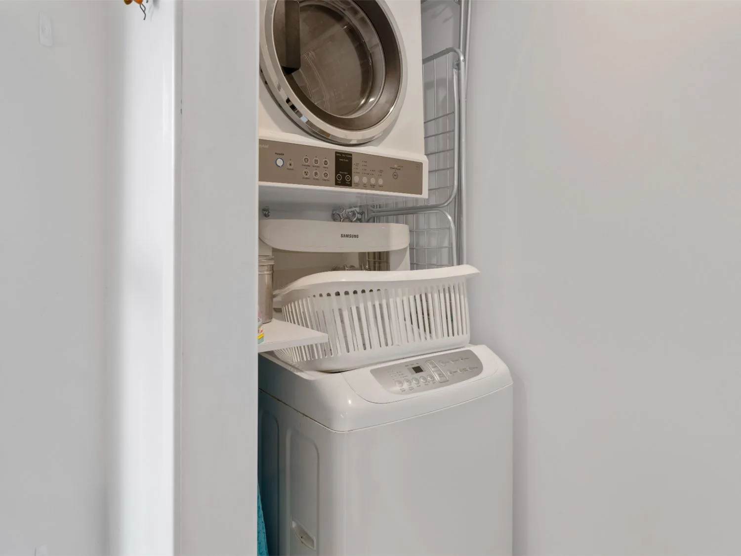 Una zona de lavandería con electrodomésticos apilados y una lavadora blanca de carga superior.