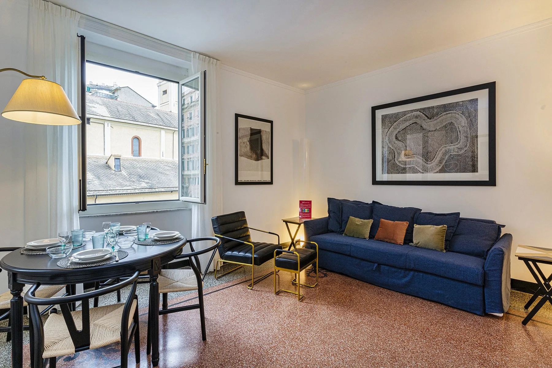 A living room with a blue sofa and a dining table beside an open window.