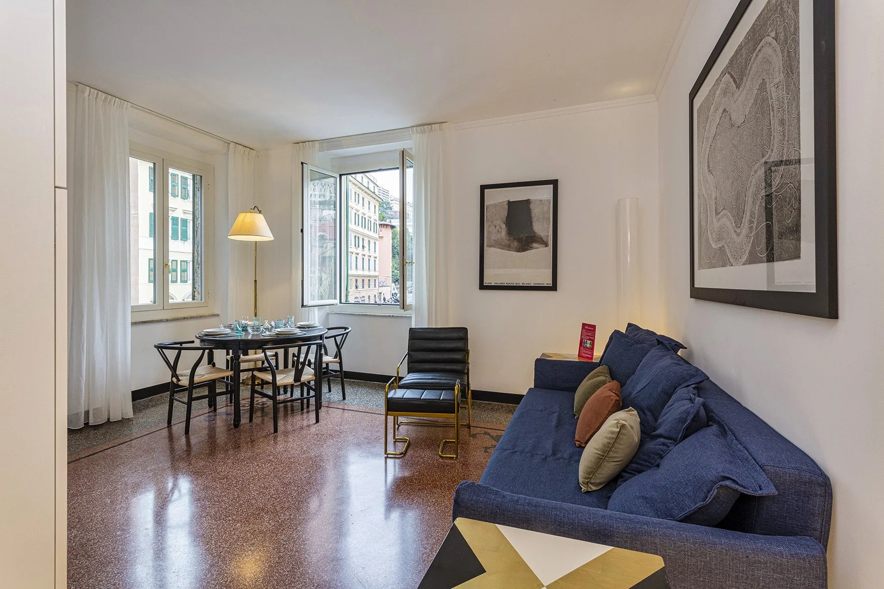 Una sala de estar con asientos azules y una mesa de comedor junto a las ventanas.