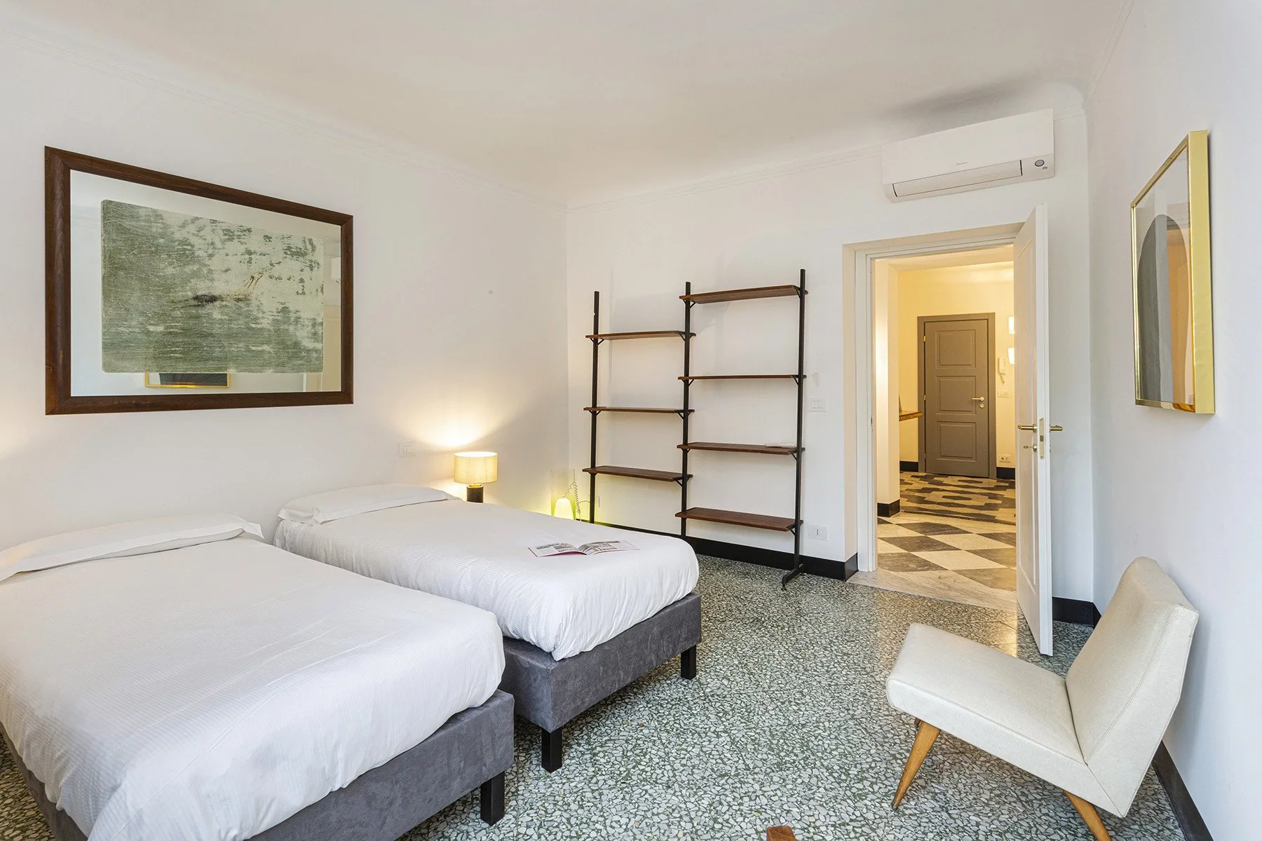 A bedroom with two beds, open shelving, and a chair.