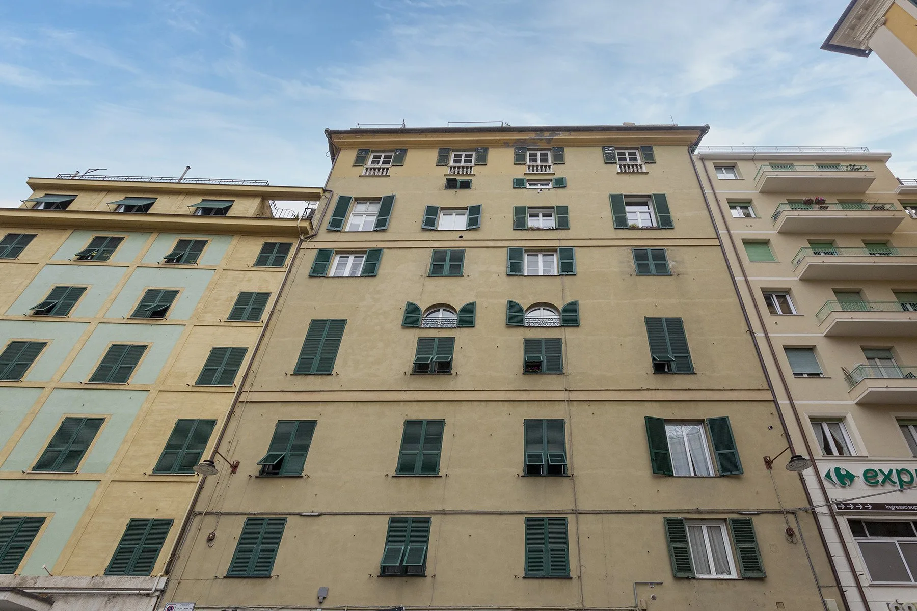 Una hilera de edificios de varias plantas con ventanas con contraventanas bajo un cielo azul.